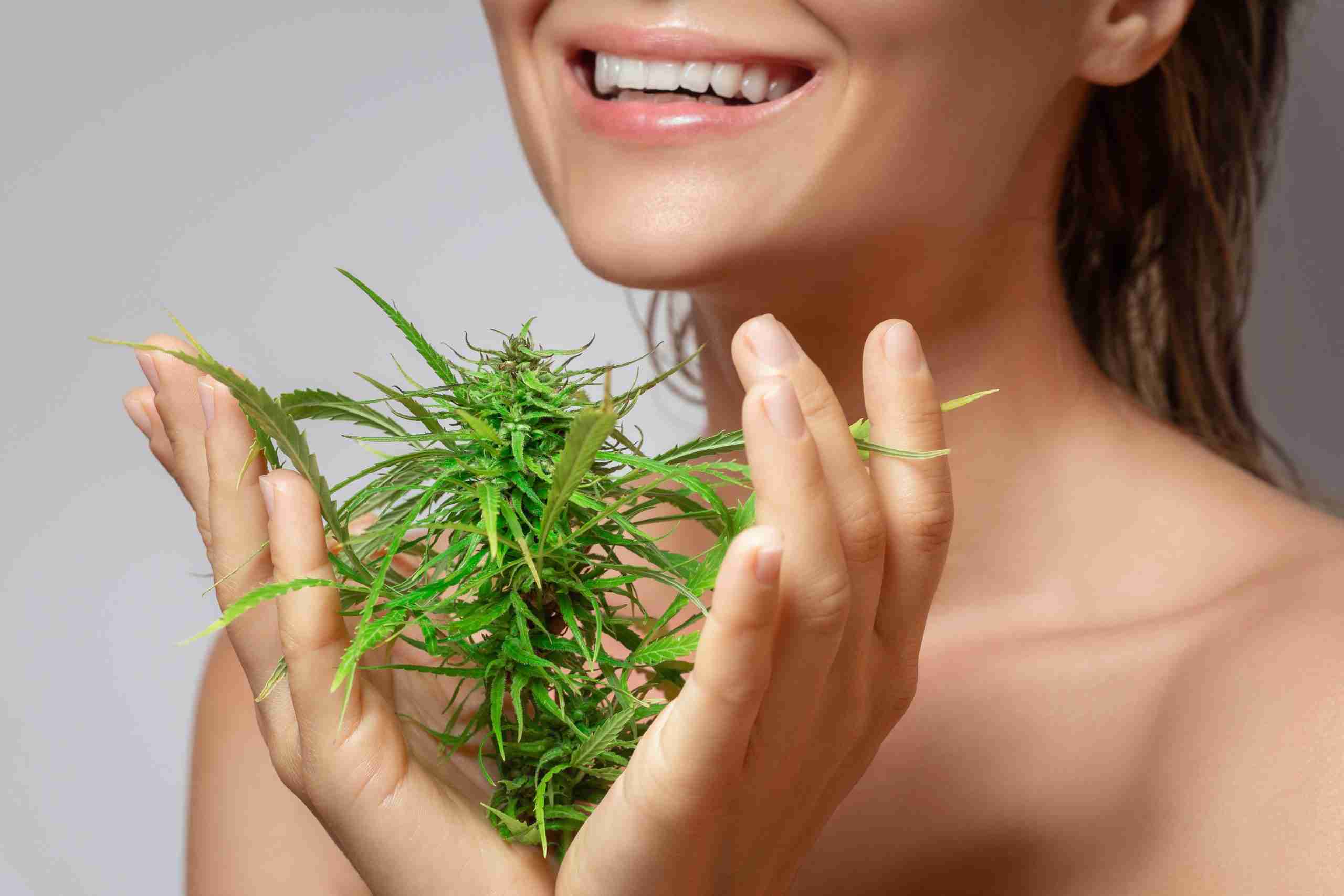 CBD cosmetics concept. Beautiful woman with a cannabis leaf on gray background